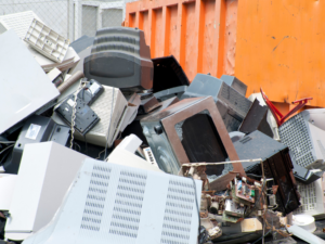 A pile of old electronic equipment inside an orange dumpster
