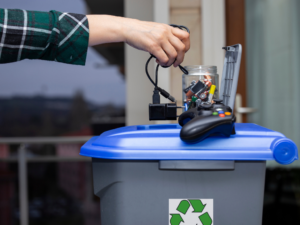 A man in a plaid shirt throwing electronics into a recycling container