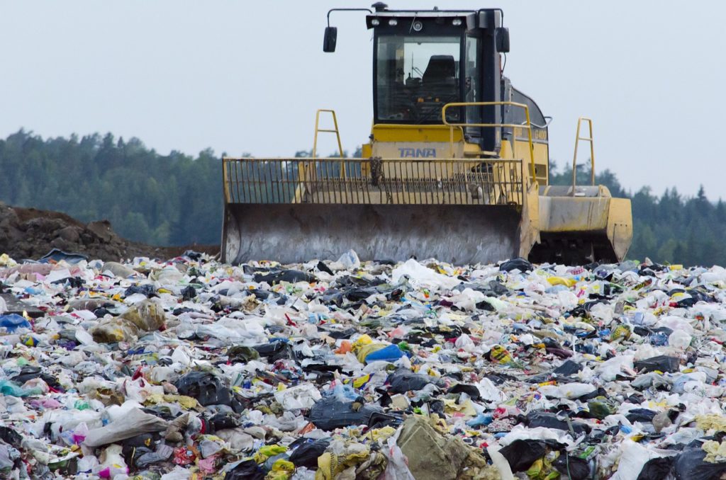 A bulldozer driving across piles of waste at a landfill.