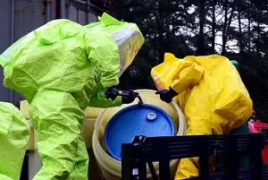 Two people in hazmat suits handling a barrel of toxic waste